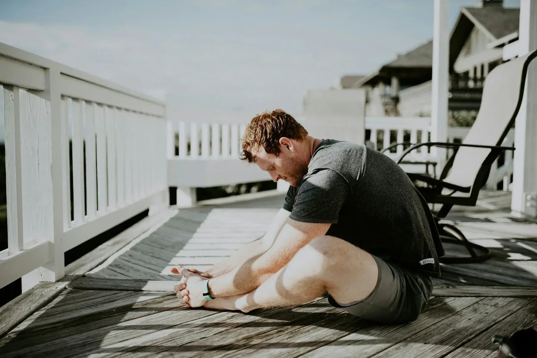 Man stretching forward while sitting on a wooden deck outdoors