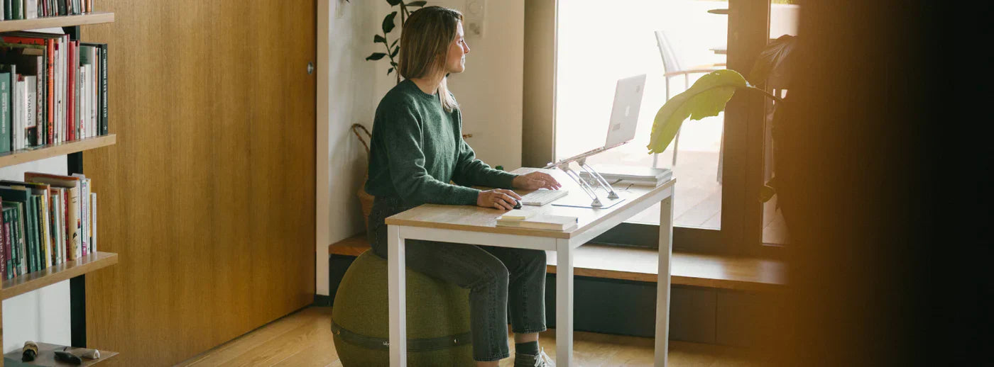 Woman working at a desk on a laptop while sitting on a green Bloon ergonomic ball chair