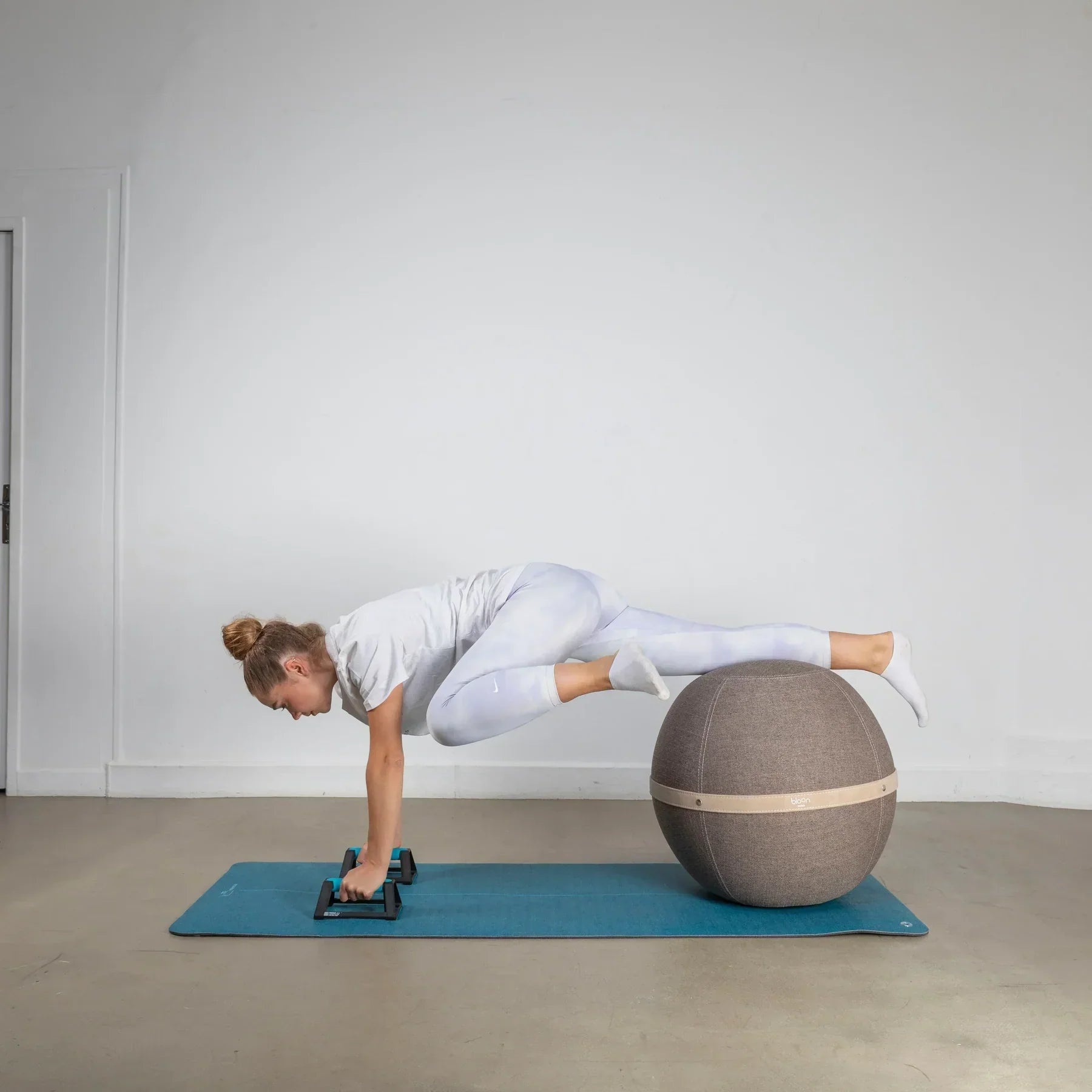 Woman doing core exercise with hands on push-up bars and legs supported by a stability ball