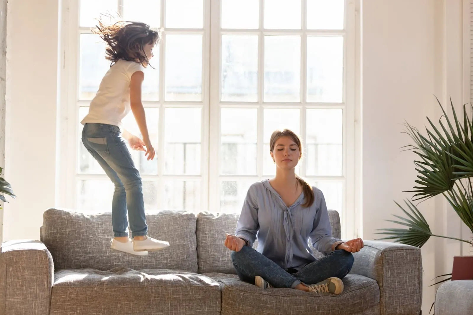 Manage hyperactivity in children : a mother doing relaxation while her daughter is jumping on the couch