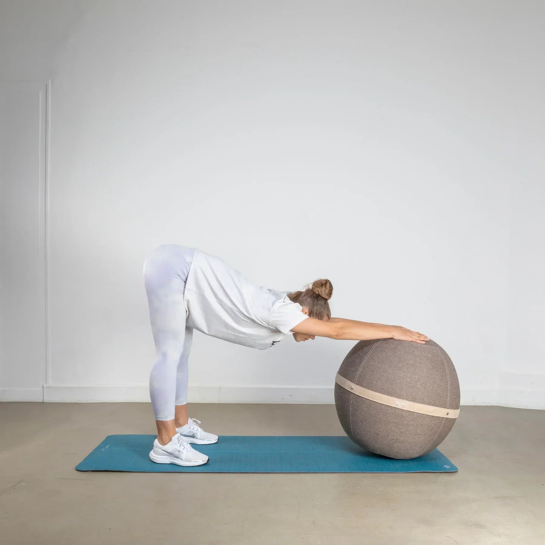 Woman stretching her back while holding onto an exercise ball on a yoga mat